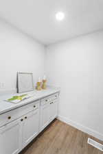 Bar with white cabinets, light wood-style floors, and light stone counters