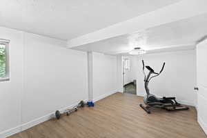 Exercise room with a textured ceiling and light wood-type flooring