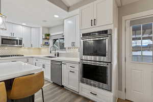Kitchen with white cabinets, appliances with stainless steel finishes, open shelves, hanging light fixtures, and recessed lighting