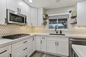 Kitchen with open shelves, appliances with stainless steel finishes, white cabinets, light stone countertops, and tasteful backsplash