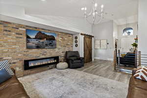 Living area with light wood finished floors, a barn door, high vaulted ceiling, a fireplace, and a chandelier