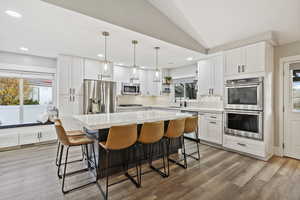 Kitchen featuring healthy amount of natural light, white cabinetry, decorative light fixtures, vaulted ceiling, and recessed lighting