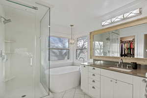 Bathroom with vanity, a walk in closet, a freestanding bath, a stall shower, and light marble finish flooring