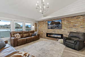 Living room with lofted ceiling, wood finished floors, brick wall, a brick fireplace, and a chandelier