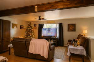 Living area featuring wood finished floors, beamed ceiling, a ceiling fan, and a textured ceiling