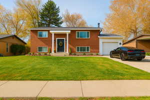 Raised ranch featuring brick siding, a front yard, an attached garage, and concrete driveway