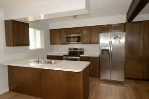 Kitchen featuring a peninsula, appliances with stainless steel finishes, light countertops, light wood-type flooring, and dark brown cabinetry