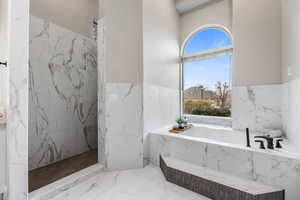 Bathroom with marble tiled flooring, wainscoting, a marble finish shower, and a garden tub