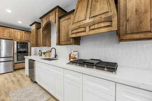 Kitchen with appliances with stainless steel finishes, light stone counters, backsplash, custom range hood, and light wood finished floors