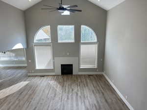 Unfurnished living room with ceiling fan, a fireplace, light wood-style floors, and high vaulted ceiling
