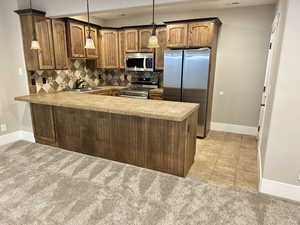 Kitchen with backsplash, stainless steel appliances, a peninsula, decorative light fixtures, and light carpet