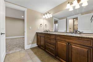 Bathroom with double vanity, dark colored carpet, and dark tile patterned flooring