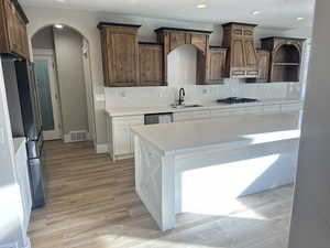 Kitchen featuring stainless steel appliances, decorative backsplash, a textured ceiling, light wood finished floors, and arched walkways