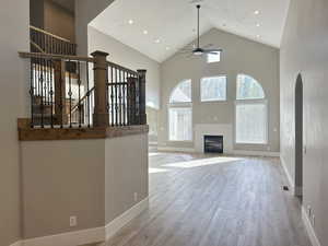 Unfurnished living room featuring high vaulted ceiling, ceiling fan, a glass covered fireplace, wood finished floors, and recessed lighting