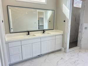 Bathroom featuring light marble finish floors, double vanity, plenty of natural light, and a marble finish shower