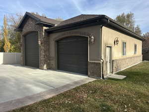 View of side of home with a garage, stucco siding, concrete driveway, stone siding, and roof with shingles