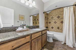 Bathroom featuring vanity, shower / bath combination with curtain, and dark stone finish floors