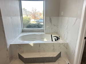 Bathroom featuring light marble finish floors and a garden tub