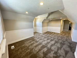 Additional living space with dark colored carpet, a textured ceiling, lofted ceiling, recessed lighting, and ceiling fan