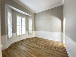 Unfurnished room with wood finished floors, crown molding, and arched walkways
