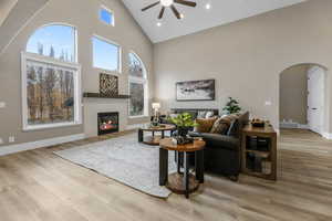 Living room featuring high vaulted ceiling, arched walkways, a glass covered fireplace, a ceiling fan, and light wood finished floors