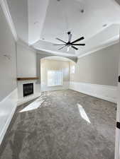 Unfurnished living room featuring a tray ceiling, carpet floors, ornamental molding, a large fireplace, and arched walkways