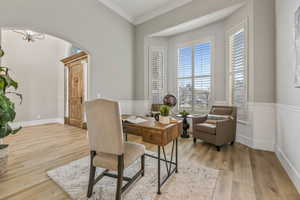 Office space with arched walkways, light wood-style flooring, and crown molding