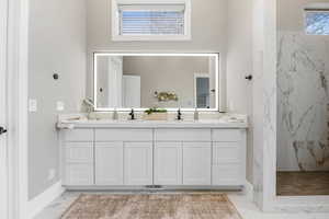 Bathroom featuring light marble finish flooring, double vanity, and a marble finish shower