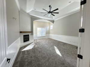 Unfurnished living room with a tray ceiling, dark colored carpet, ornamental molding, arched walkways, and a large fireplace