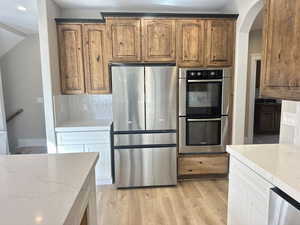 Kitchen with stainless steel appliances, light wood-style floors, light stone countertops, decorative backsplash, and arched walkways