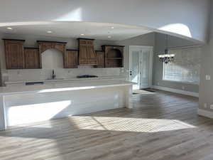 Kitchen featuring decorative backsplash, light wood-type flooring, light stone counters, custom range hood, and a chandelier