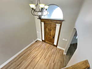 Entryway with light wood-style floors, a chandelier, arched walkways, and a towering ceiling