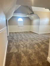 Additional living space with a textured ceiling, carpet flooring, vaulted ceiling, a wainscoted wall, and ceiling fan