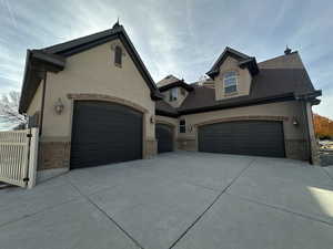 French country inspired facade with brick siding, concrete driveway, stucco siding, a shingled roof, and a garage