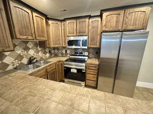 Kitchen featuring stainless steel appliances, decorative backsplash, tile counters, brown cabinetry, and light tile patterned flooring