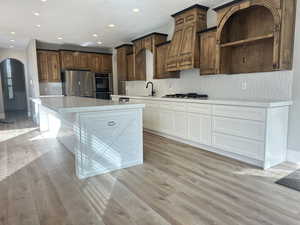 Kitchen with white cabinetry, backsplash, a kitchen island, light wood finished floors, and recessed lighting