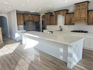 Kitchen with arched walkways, tasteful backsplash, recessed lighting, light stone counters, and stainless steel appliances
