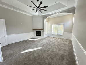 Unfurnished living room with a tray ceiling, crown molding, carpet, a fireplace, and arched walkways