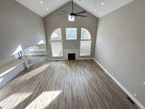 Unfurnished living room featuring high vaulted ceiling, wood finished floors, a fireplace, recessed lighting, and a ceiling fan