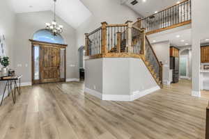 Entrance foyer featuring arched walkways, high vaulted ceiling, light wood-type flooring, a chandelier, and stairway