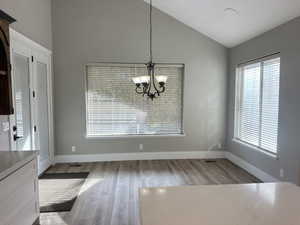 Unfurnished dining area featuring light wood-style flooring, a chandelier, and high vaulted ceiling
