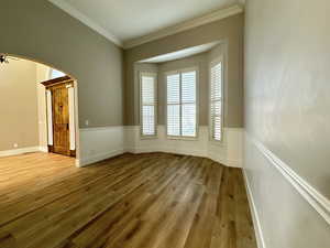 Unfurnished room with arched walkways, light wood-style floors, and crown molding