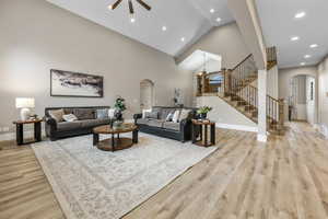 Living room with arched walkways, stairs, light wood-type flooring, high vaulted ceiling, and recessed lighting