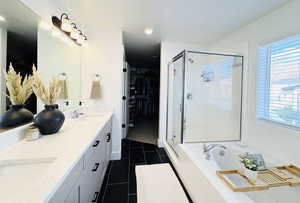 Full bath with a spacious closet, double vanity, a garden tub, a shower stall, and dark tile patterned flooring