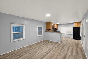 Kitchen with light wood-type flooring, a peninsula, freestanding refrigerator, brown cabinetry, and a textured ceiling