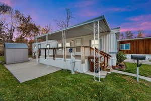Back of house at dusk featuring a lawn, a shed, a porch, and a patio