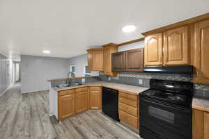 Kitchen with black appliances, brown cabinetry, a peninsula, light wood-style flooring, and tasteful backsplash