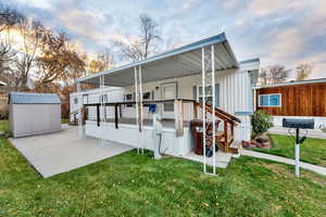 Rear view of house with a lawn, a storage shed, a wooden deck, and a patio