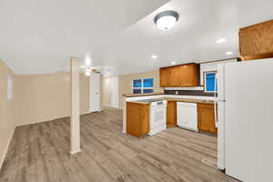 Kitchen featuring white appliances, a peninsula, brown cabinetry, open floor plan, and light wood-style floors