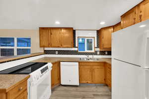 Kitchen with white appliances, decorative backsplash, light wood-type flooring, brown cabinets, and light countertops
